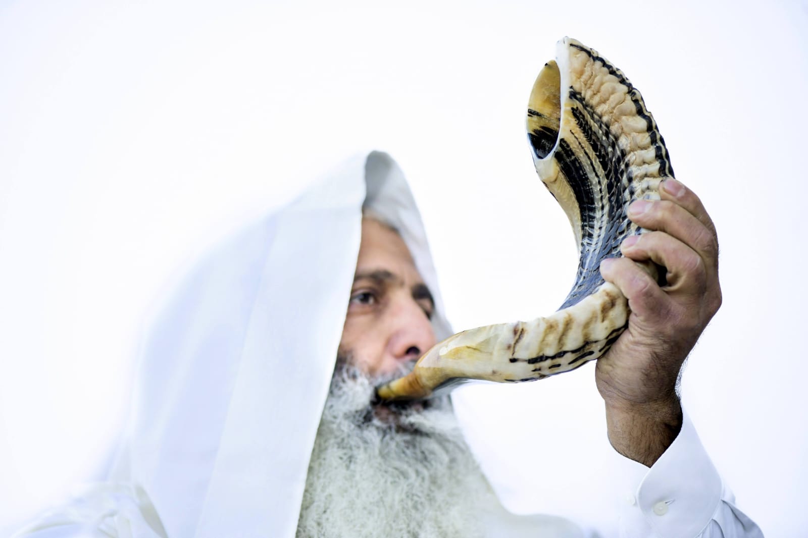 Man blowing a shofar against a white background